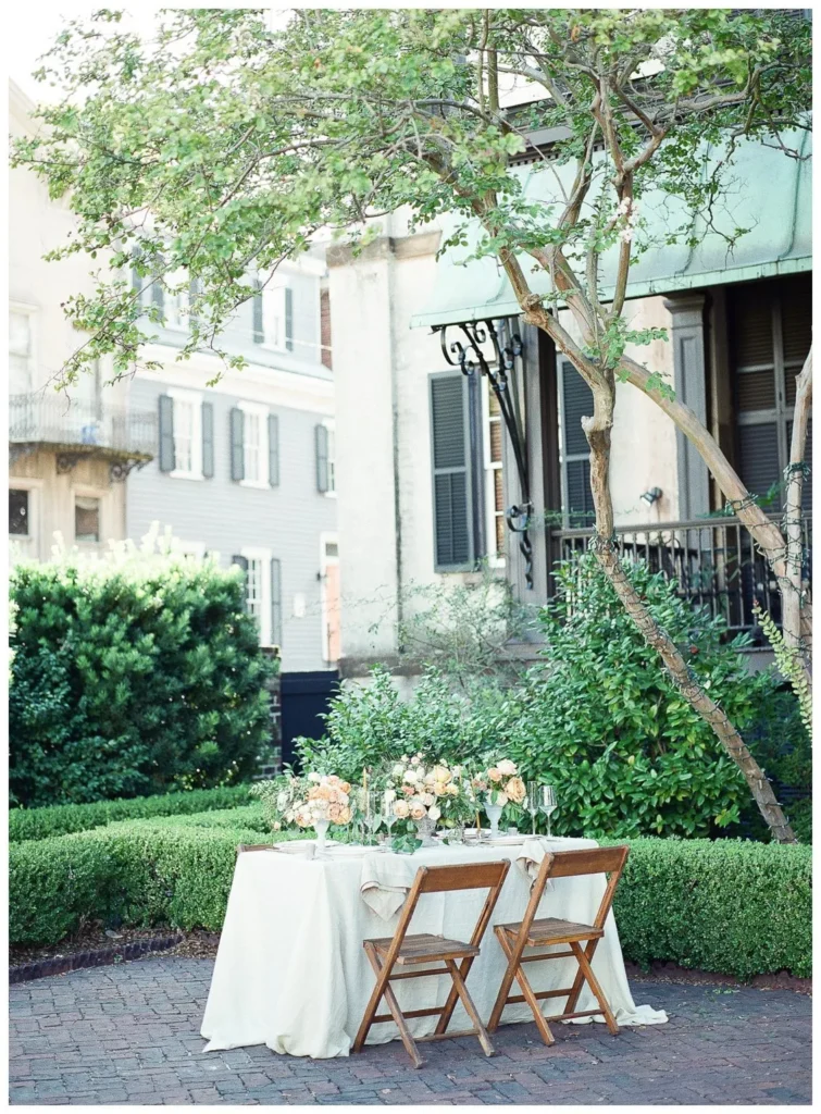 Photographers Guide To Showit Image Optimization Two-person table set with white linens, floral centerpieces, and wooden chairs in a garden courtyard beside historic townhouses