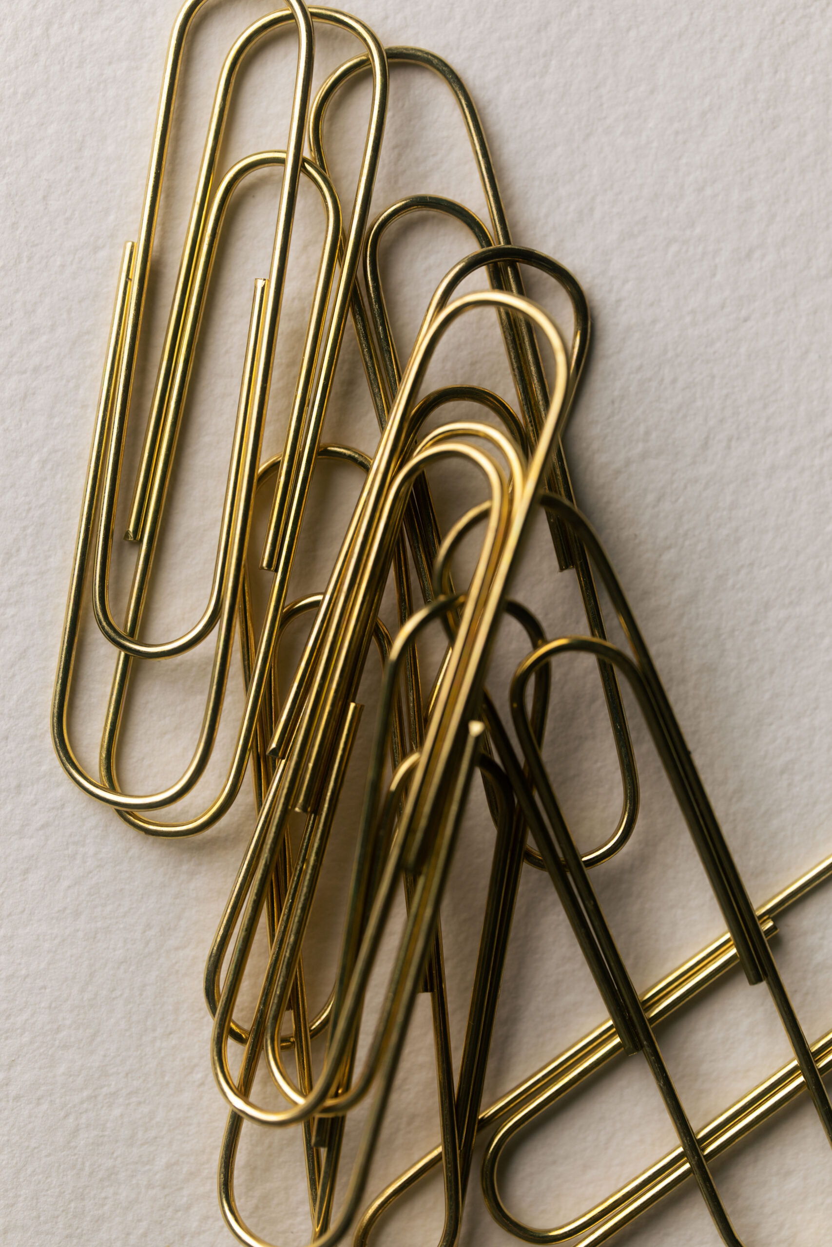 Close-up of several gold-colored paper clips loosely stacked on a textured white surface