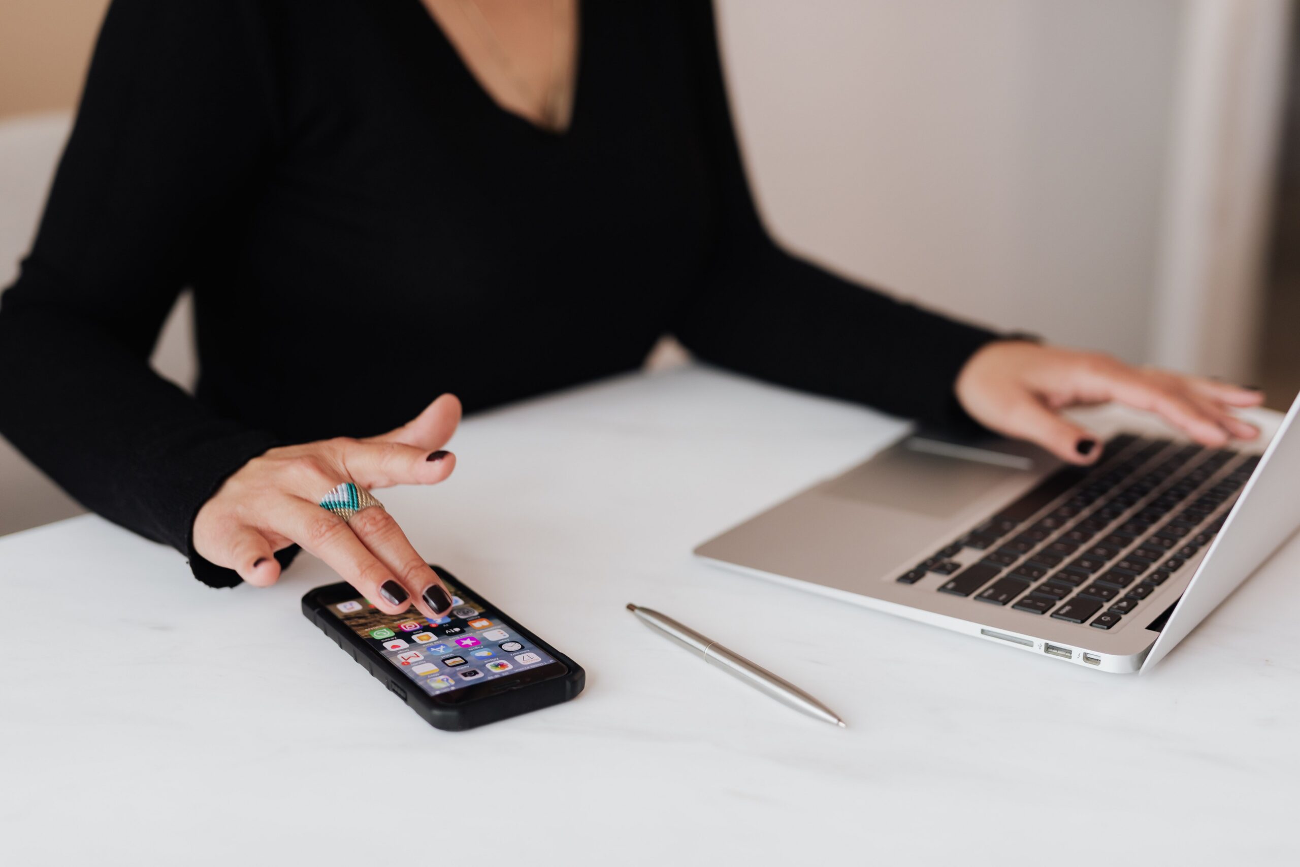 Woman using a smartphone with one hand while typing on a laptop with the other