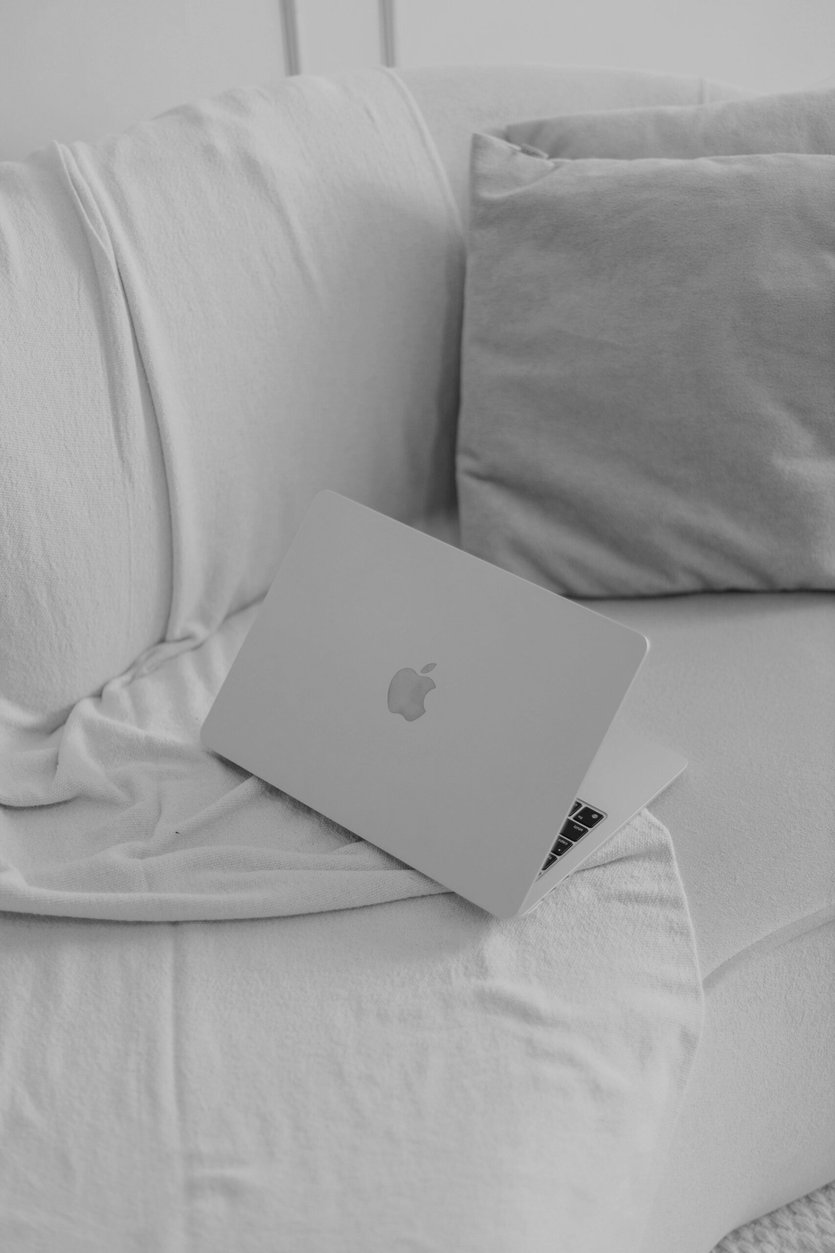 Apple macbook laptop resting open on a bed with white bedding and pillows