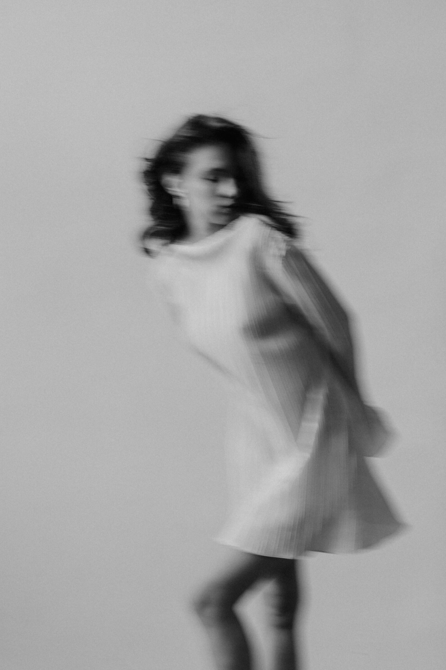Black-and-white motion-blurred figure of a woman in a flowing dress, conveying movement and fluidity
