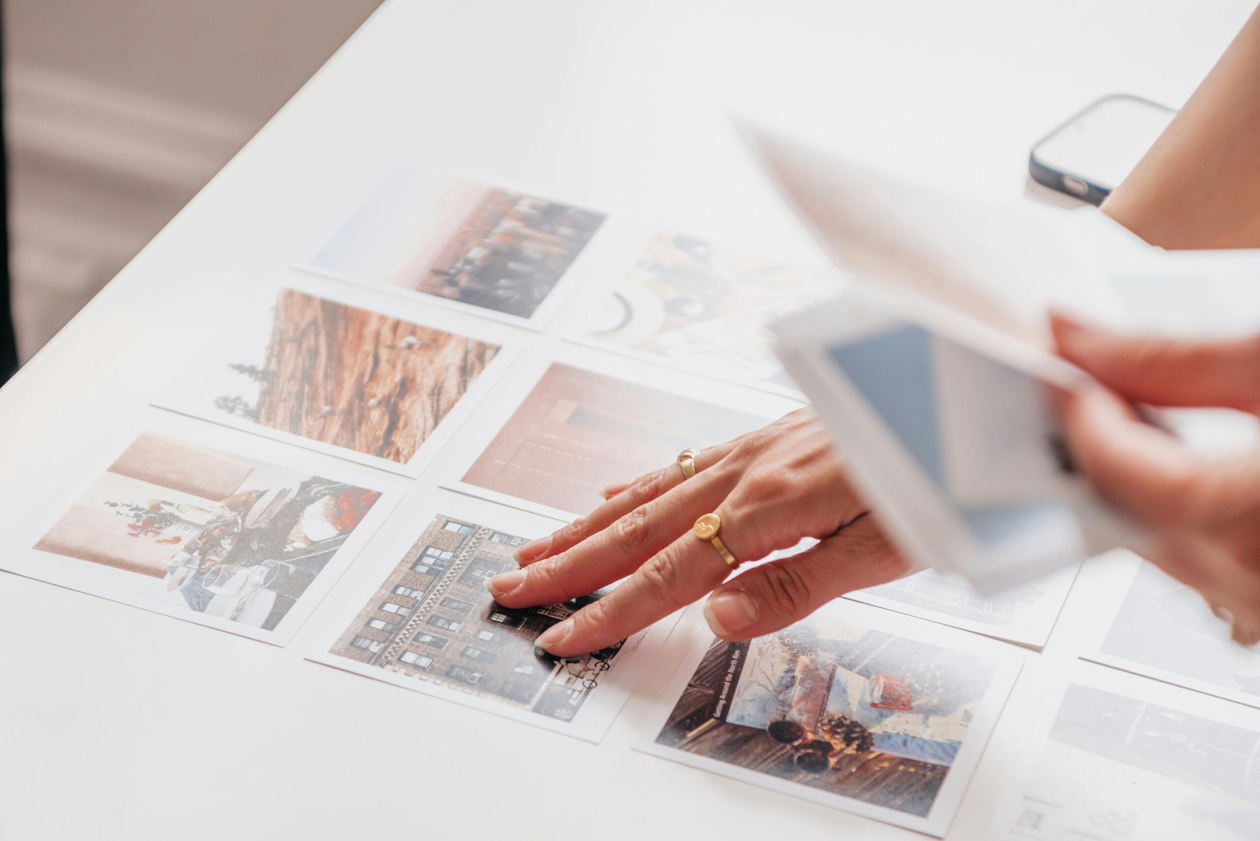 Hands arranging printed photo prints laid out in a grid on a white table