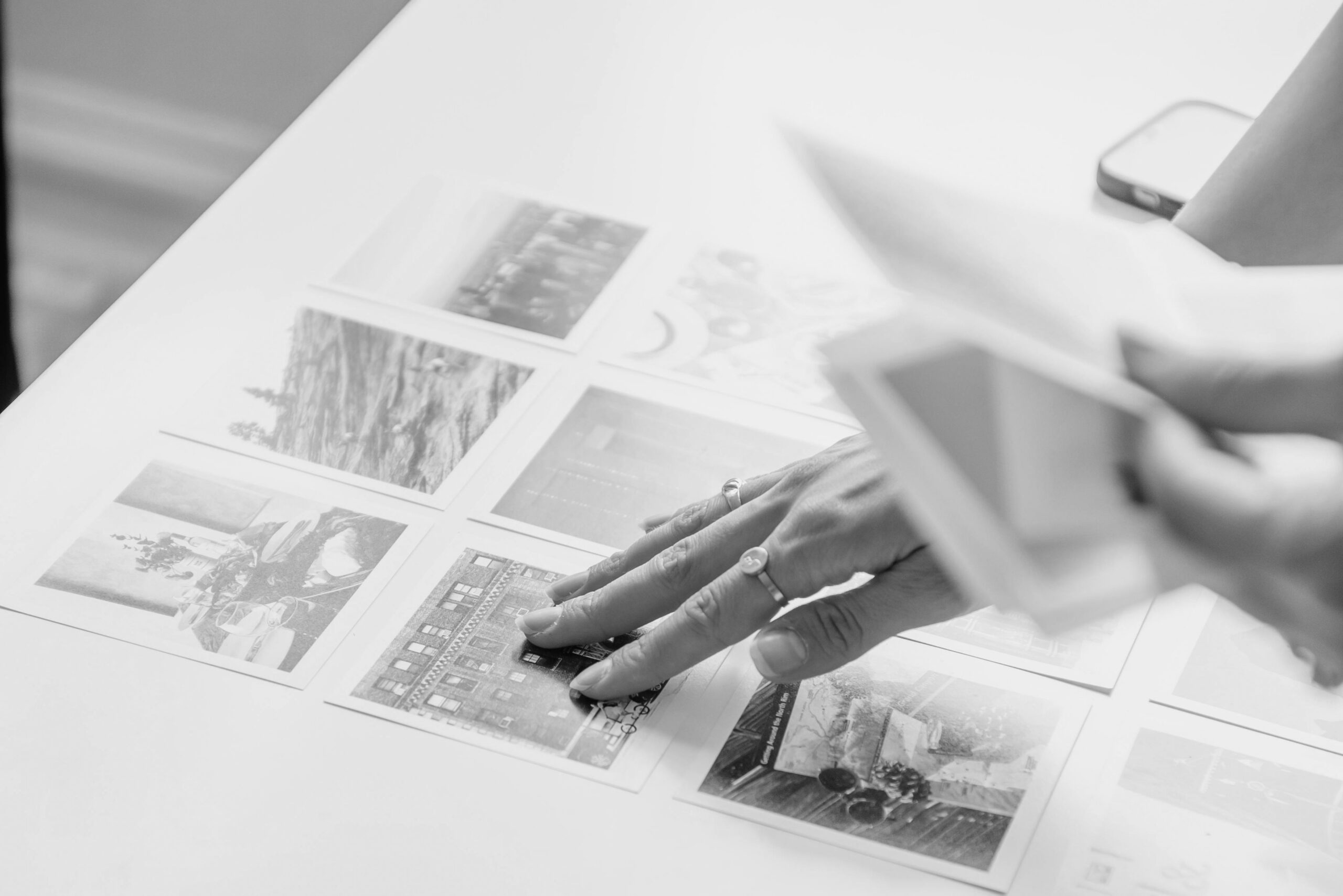Hands sorting through a collection of printed photographs spread out on a white table