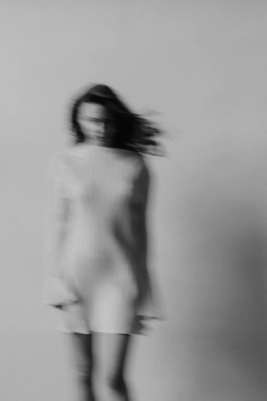 Black-and-white motion-blurred figure of a woman in a white dress, conveying movement