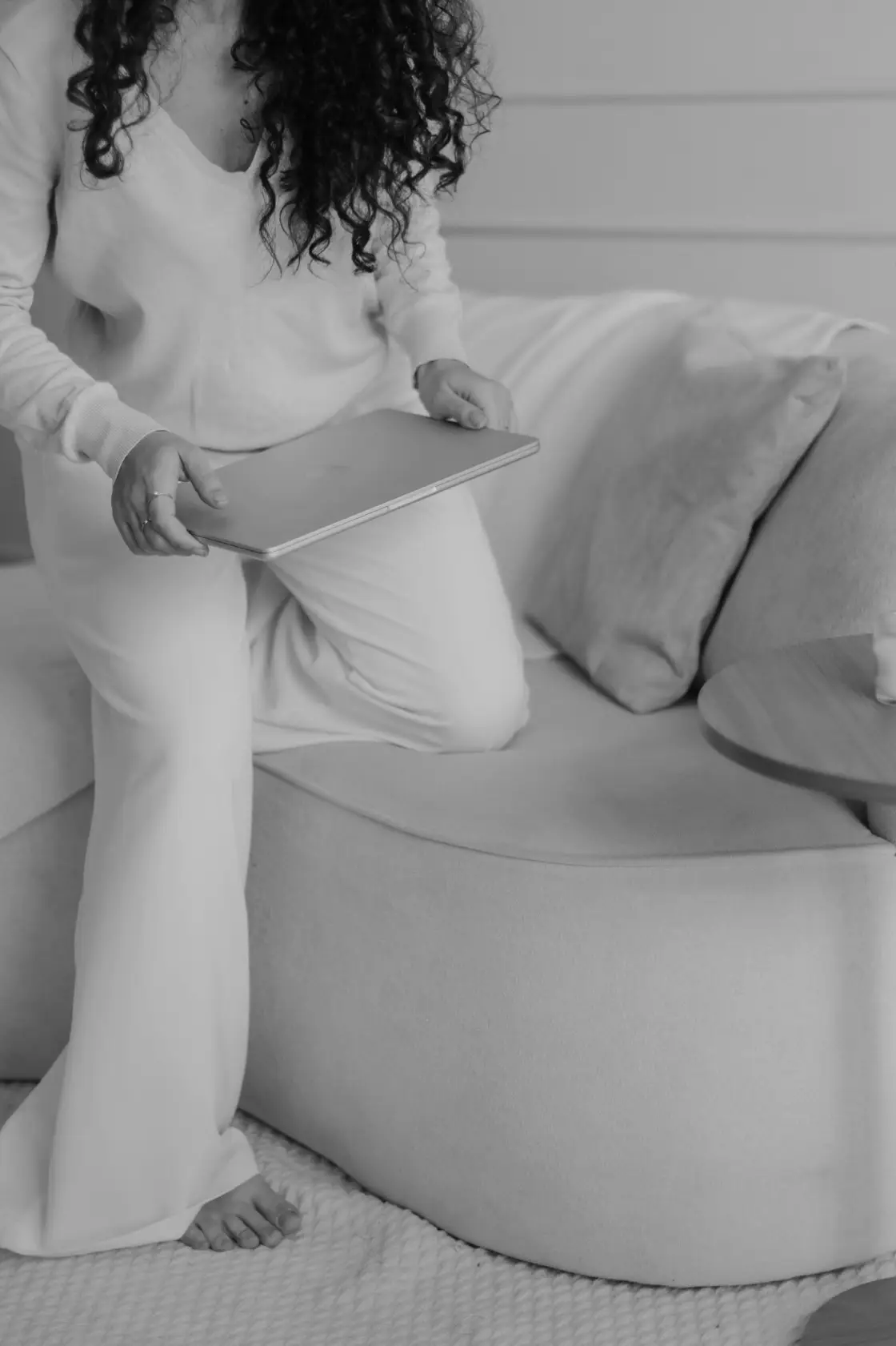 Woman in casual loungewear sitting on a sofa, holding a tablet or laptop