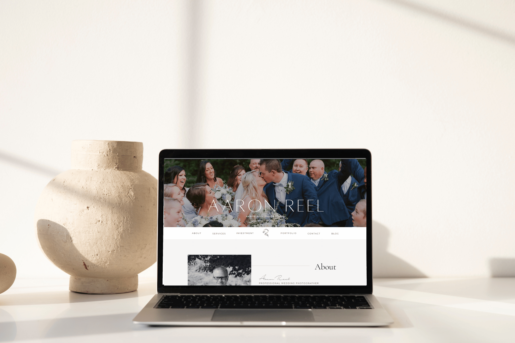 Laptop displaying the aaron reel photography website homepage, featuring a wedding party hero image and an about section